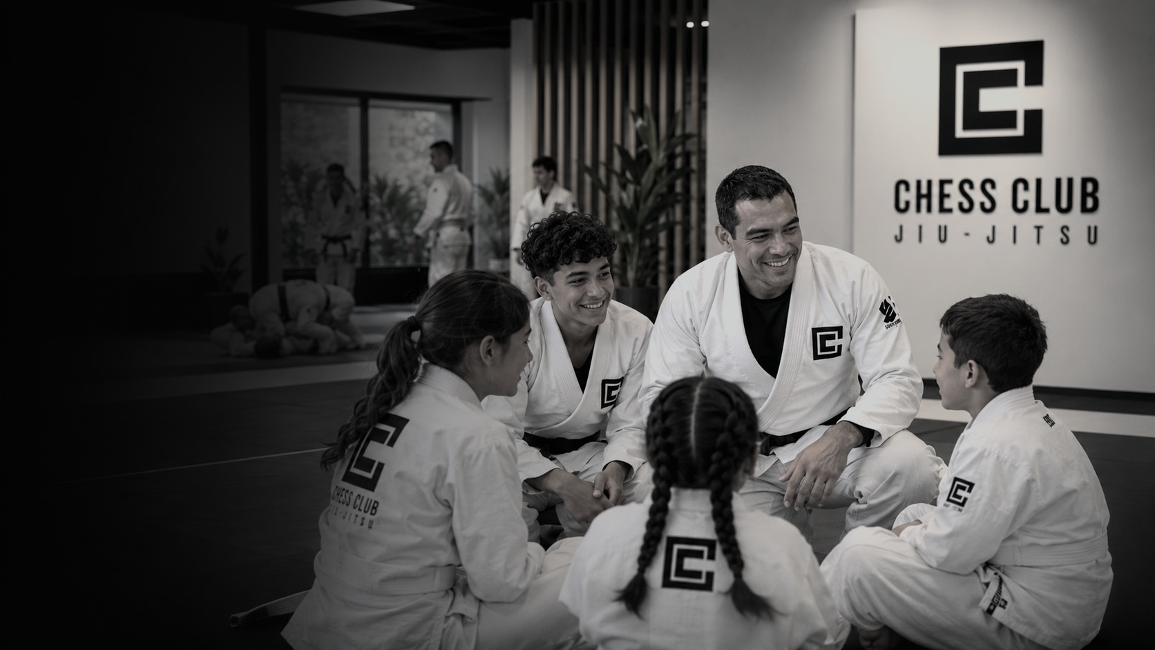 Coach and students sharing a relaxed martial arts moment in the Chess Club dojo